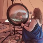 shamanic woman playing the gong for sound healing in a 6m bell tent in Portugal