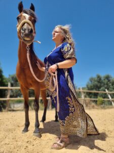 woman in her 50s standing in a strong power pose next to a horse for equine therapy